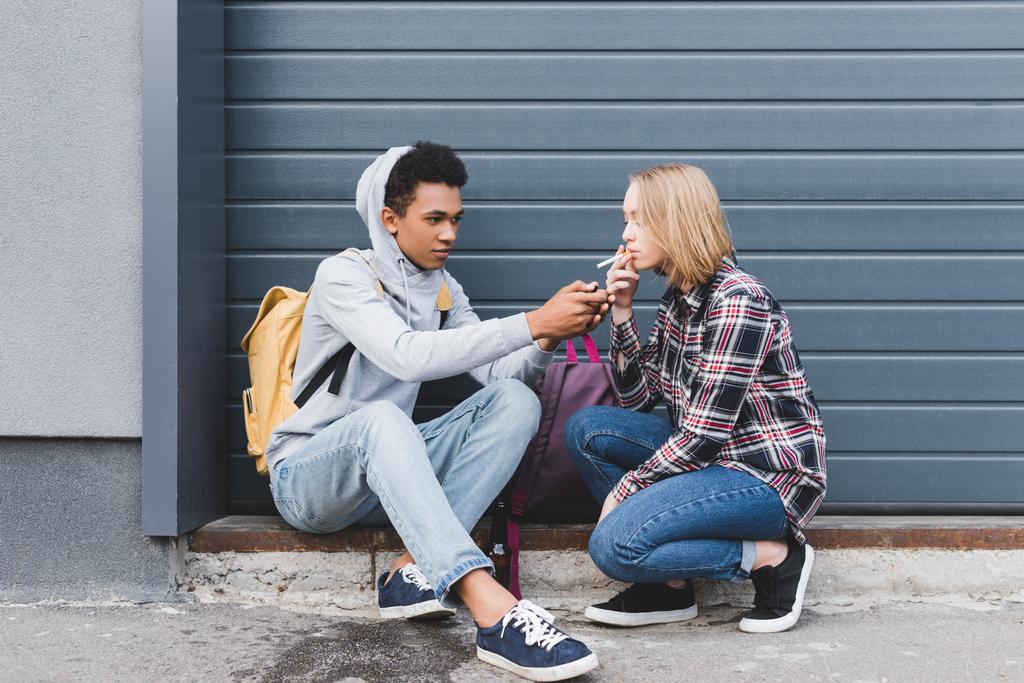 african american boy lighting cigarette of blonde and pretty teen - Photo, Image