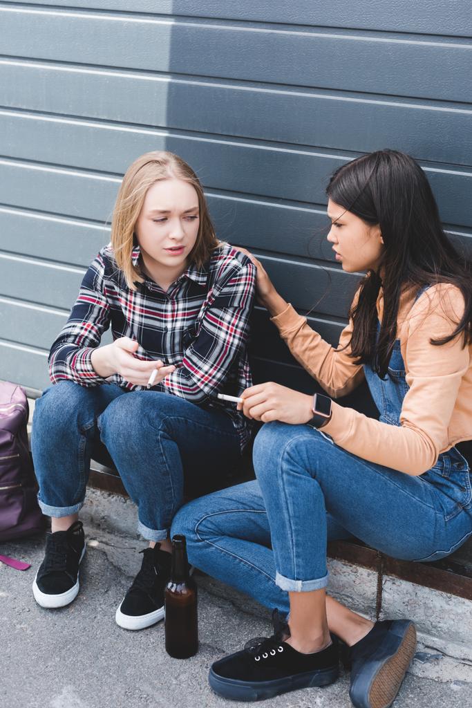 rozczarowany i ładne Nastolatki siedząc, rozmawiając i trzymając papierosy  - Zdjęcie, obraz