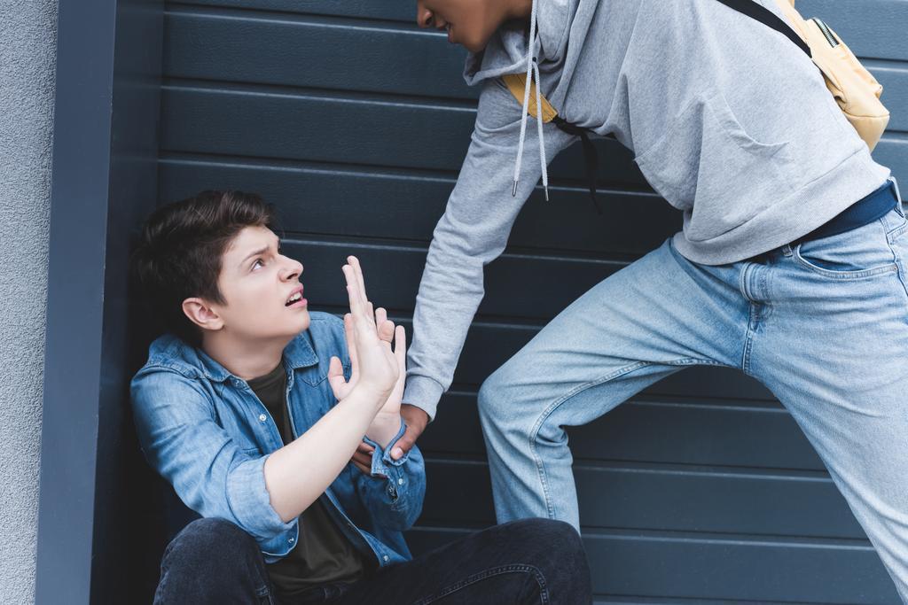 cropped view of african american boy in hoodie and jeans punching scared boy - Photo, Image