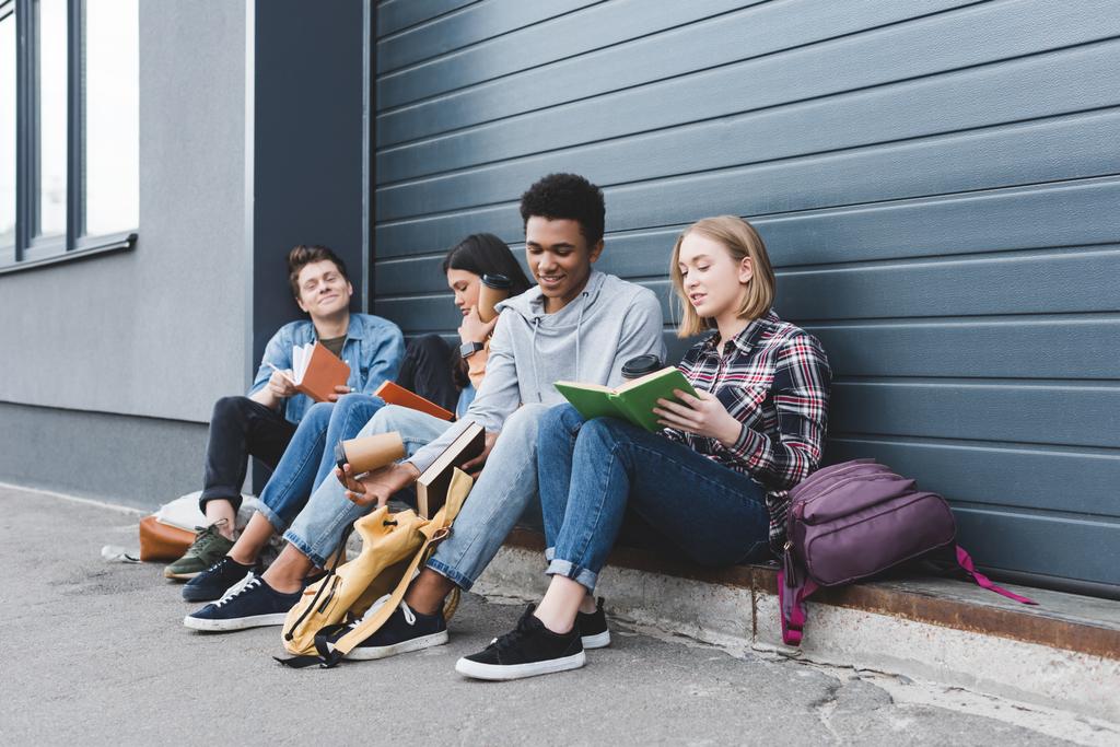 Jugendliche sitzen, reden, halten Pappbecher in der Hand und lesen Bücher  - Foto, Bild