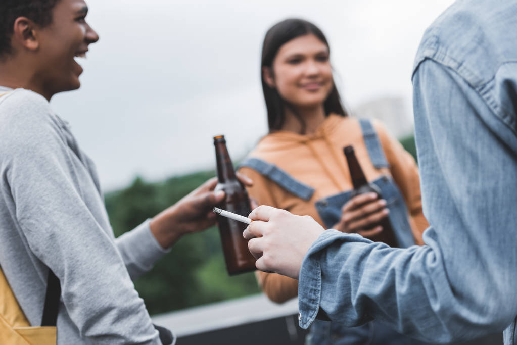 selektivní zaměření teenagerů, kteří drží skleněné láhve s pivem a kuřáckou cigaretou  - Fotografie, Obrázek