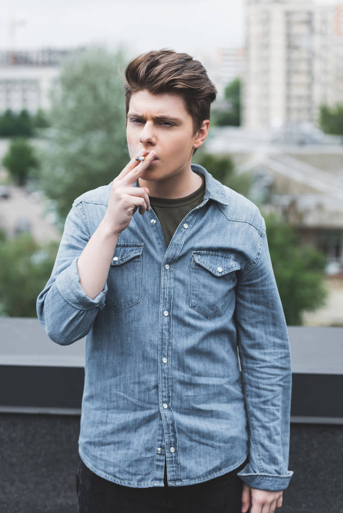 kaukázusi tini-ban denim póló dohányzás cigaretta a tetőn  - Fotó, kép