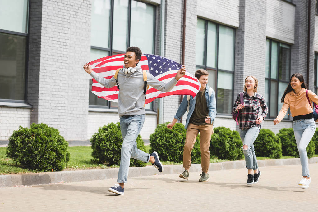 boldog tinédzserek mosolygott, gazdaság amerikai zászló és kívül futó - Fotó, kép