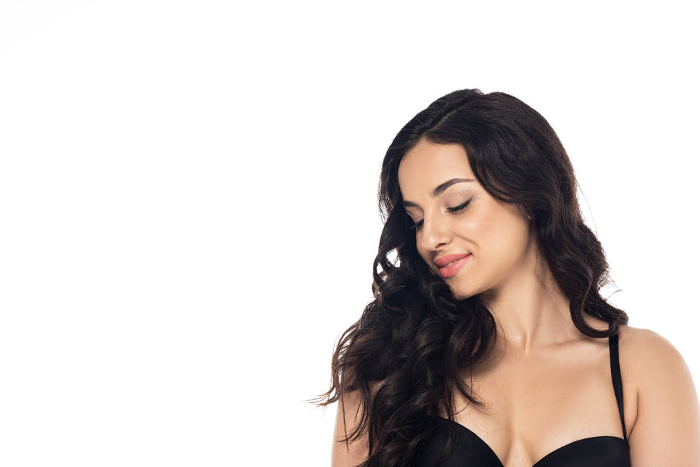 atraktivní brunetka v černé podprsence usmívající se s zavřenýma očima izolovanými na bílém - Fotografie, Obrázek