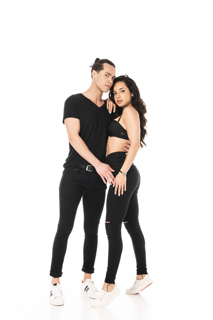 vista completa de pareja en ropa negra abrazando y mirando a la cámara aislada en blanco
 - Foto, Imagen
