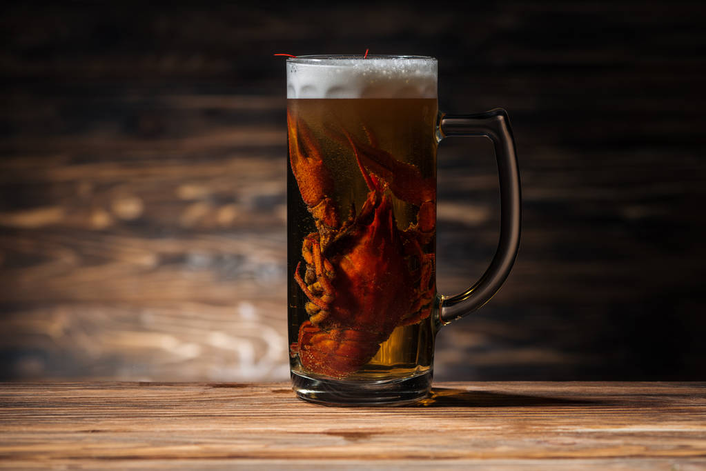 rode kreeft in glas met bier op houten oppervlak - Foto, afbeelding