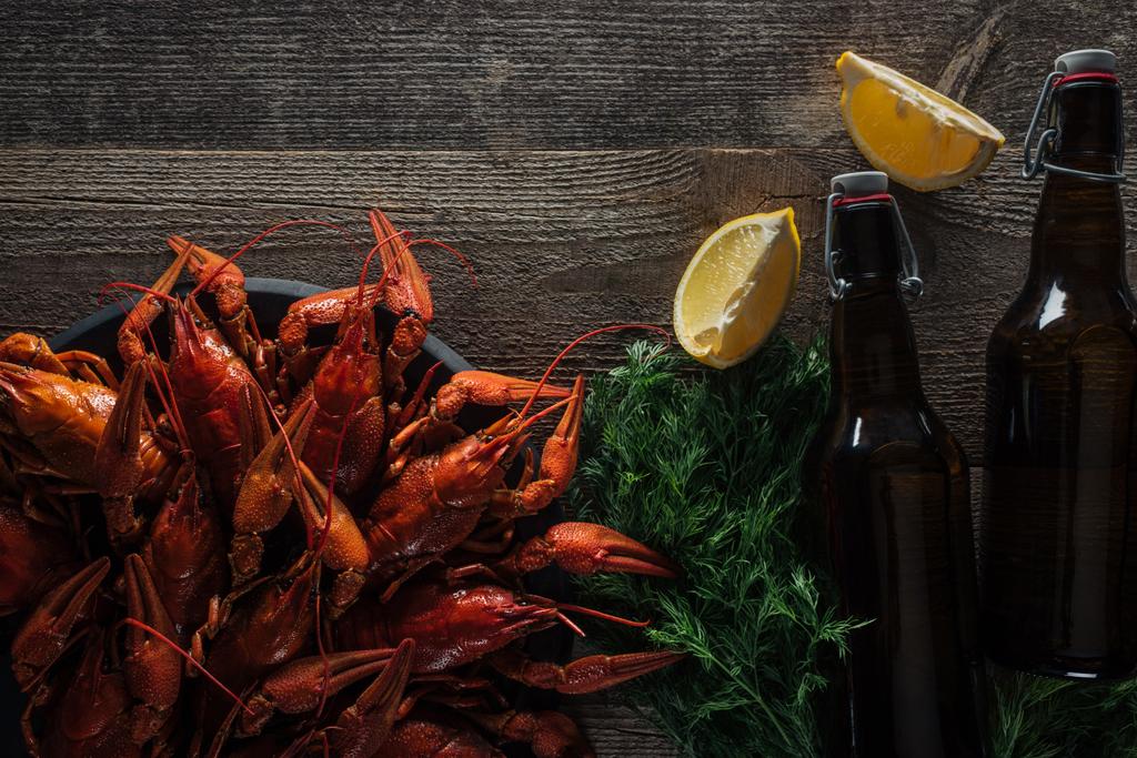 top view of red lobsters, dill, lemon slices, bottles with beer on wooden surface - Photo, Image