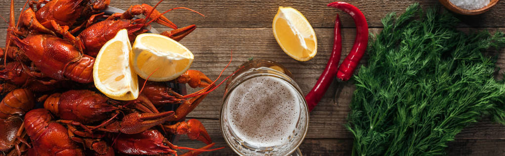 панорамний знімок червоних омарів, кропу, перцю, скибочок лимона та скла з пивом на дерев'яній поверхні
 - Фото, зображення
