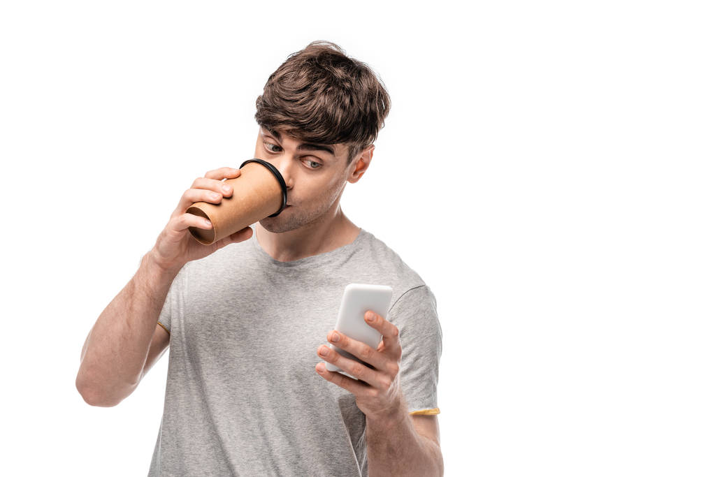 jovem bonito usando smartphone enquanto bebe café para ir isolado no branco
 - Foto, Imagem