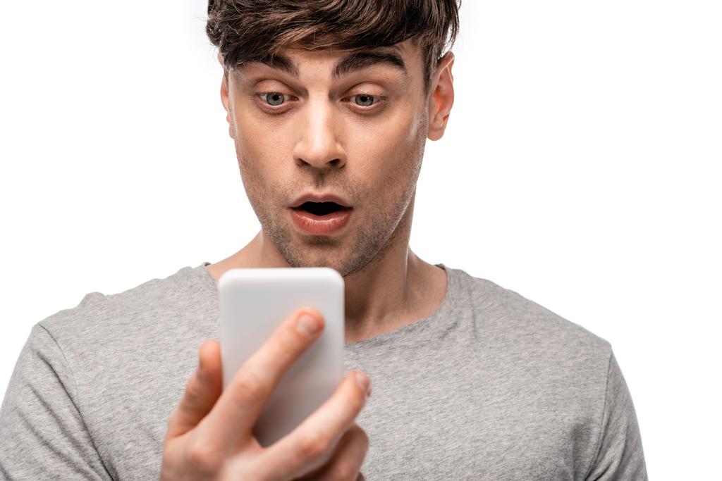красивый, удивленный молодой человек смотрит на смартфон, изолированный на белом
 - Фото, изображение