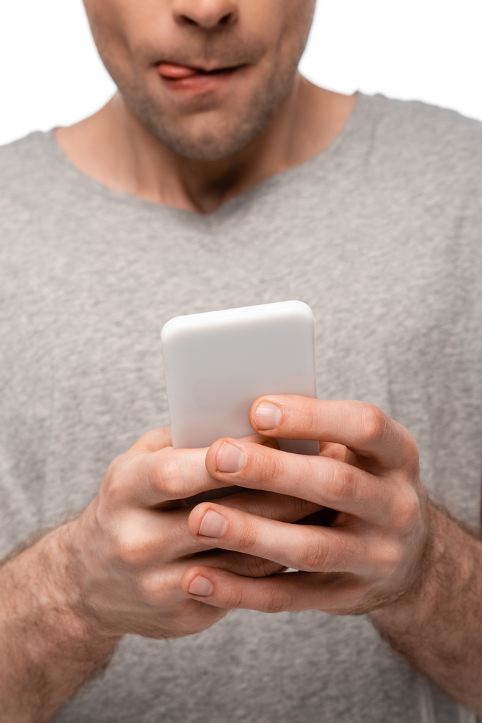 Teilansicht von Mann beim Lippenlecken während Smartphone isoliert auf weiß - Foto, Bild