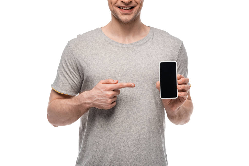 白で隔離された空白の画面でスマートフォンを指差す笑顔の男のトリミングビュー - 写真・画像