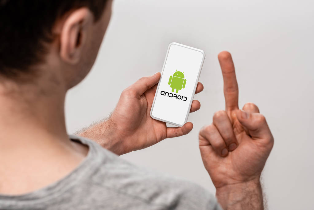KYIV, UCRANIA - 16 de mayo de 2019: vista recortada del hombre usando un teléfono inteligente con aplicación para Android y mostrando el dedo medio, aislado en gris
 - Foto, imagen