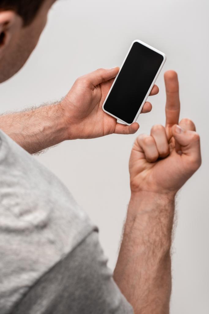 częściowy widok mężczyzny przedstawiający środkowy palec trzymając smartfon z pustym ekranem izolowanym na szaro - Zdjęcie, obraz