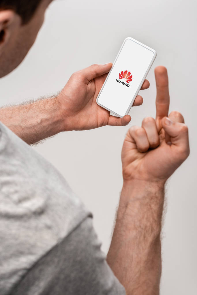 KYIV, UCRANIA - 16 DE MAYO DE 2019: vista recortada del hombre usando un teléfono inteligente con aplicación huand mostrando el dedo medio, aislado en gris
 - Foto, imagen