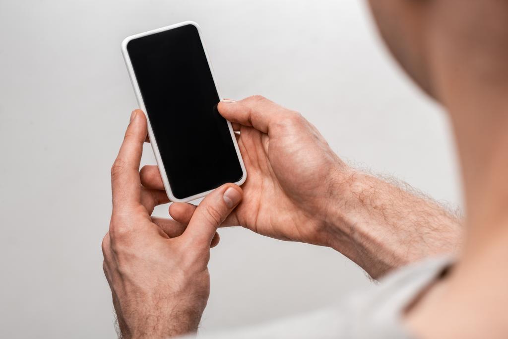 vista recortada del hombre sosteniendo teléfono inteligente con pantalla en blanco aislado en gris
 - Foto, imagen