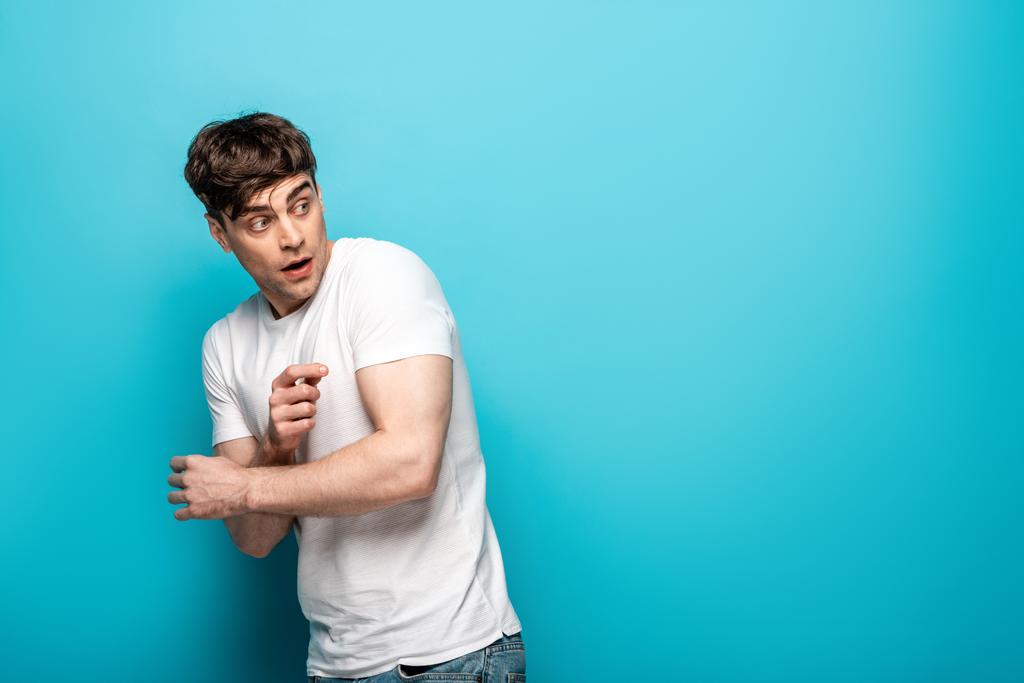 frightened young man in white t-shirt looking back on blue background - Photo, Image