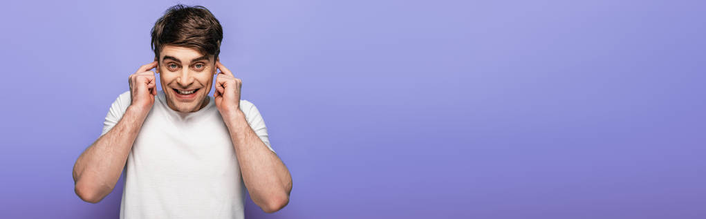 панорамный снимок веселого человека, затыкающего уши пальцами, изолированными на голубом
 - Фото, изображение