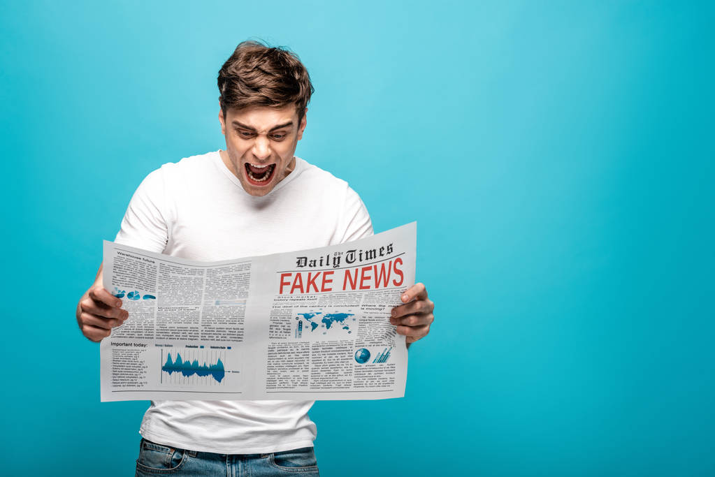hombre enojado gritando mientras lee el periódico con noticias falsas sobre fondo azul
 - Foto, Imagen