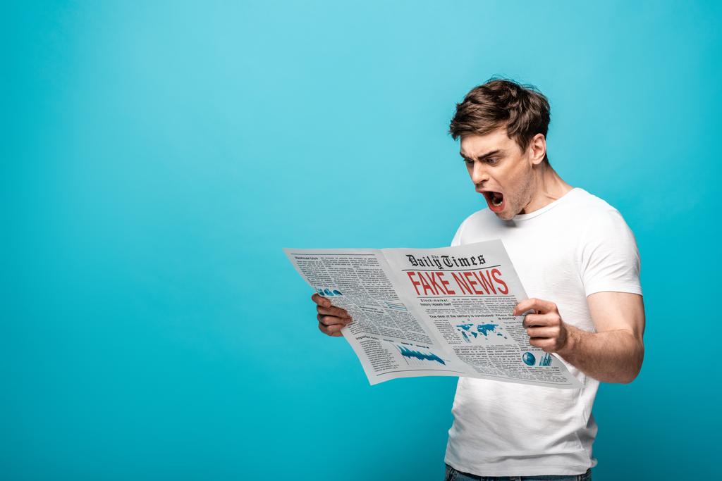 сердитий молодий чоловік читає газету з фальшивими новинами на синьому фоні
 - Фото, зображення