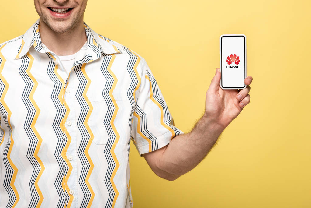 キエフ、ウクライナ - 2019年5月16日:黄色に隔離されたhuaweiアプリでスマートフォンを示す笑顔の男のトリミングビュー - 写真・画像
