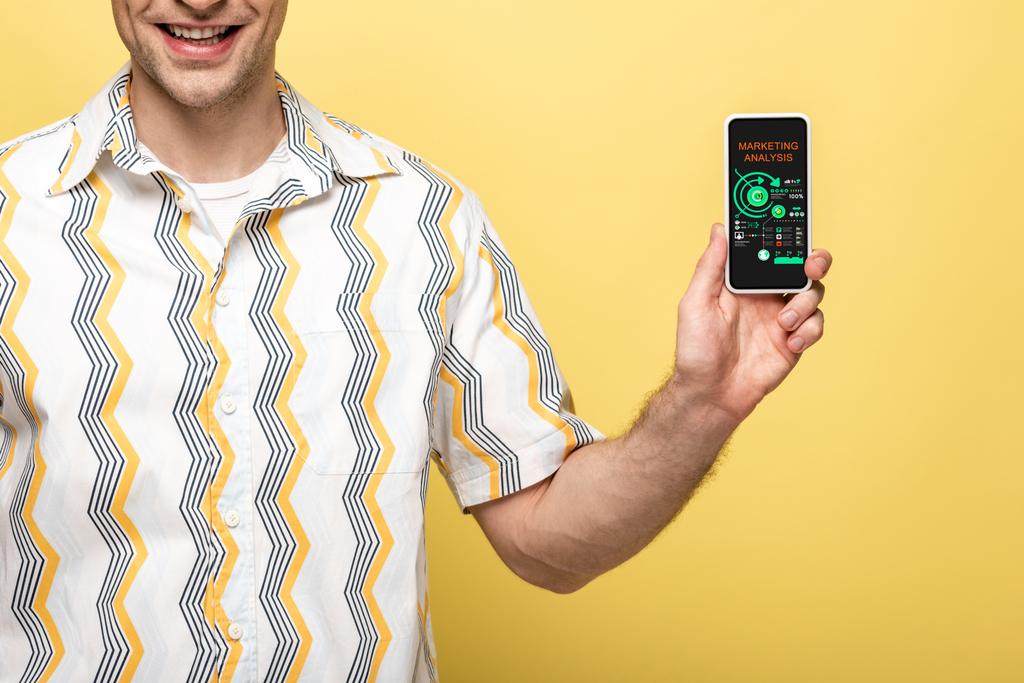 cropped view of smiling man showing smartphone with marketing analysis app, isolated on yellow - Photo, Image
