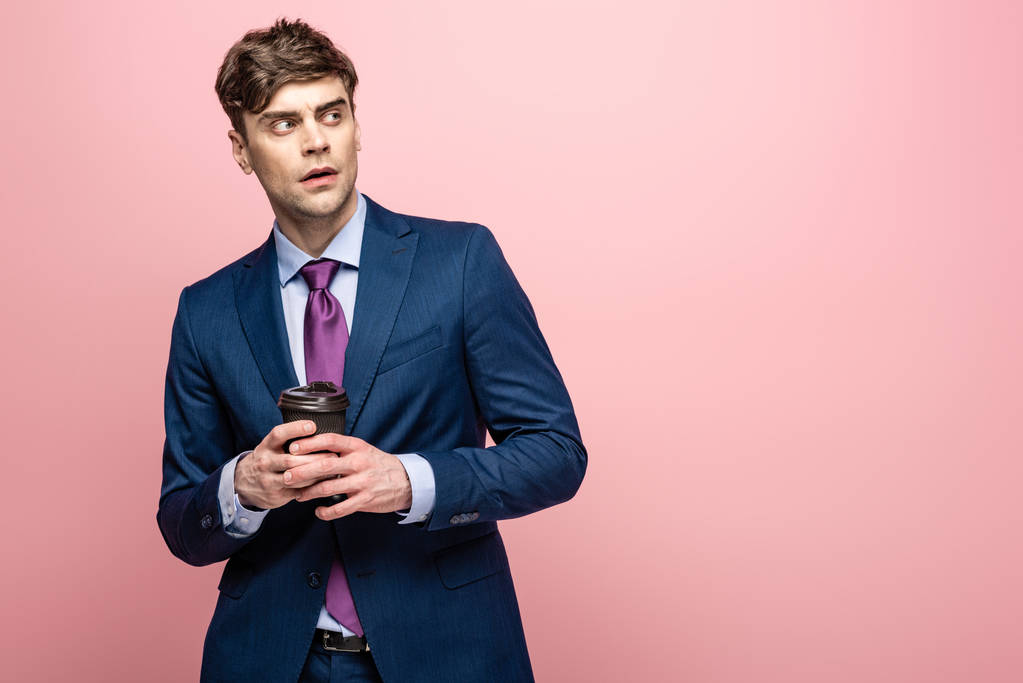 thoughtful businessman looking away while holding coffee to go on pink background - Photo, Image