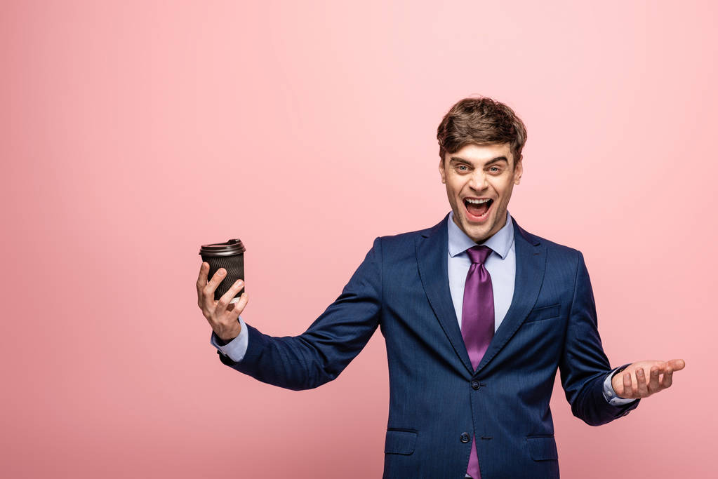 opgewonden zakenman houdt koffie te gaan terwijl lachen om camera op roze achtergrond - Foto, afbeelding