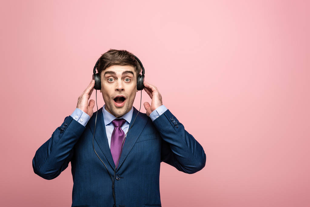 yllättynyt liikemies katselee kameraa kuunnellessaan musiikkia kuulokkeet eristetty vaaleanpunainen
 - Valokuva, kuva
