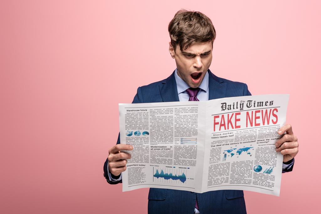 Geschockter Geschäftsmann liest Zeitung mit Fake News auf rosa Hintergrund - Foto, Bild