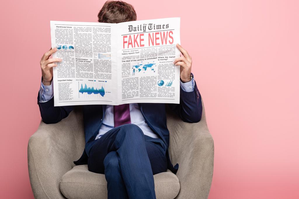 бизнесмен сидит в кресле и читает газету с фальшивыми новостями на розовом фоне
 - Фото, изображение