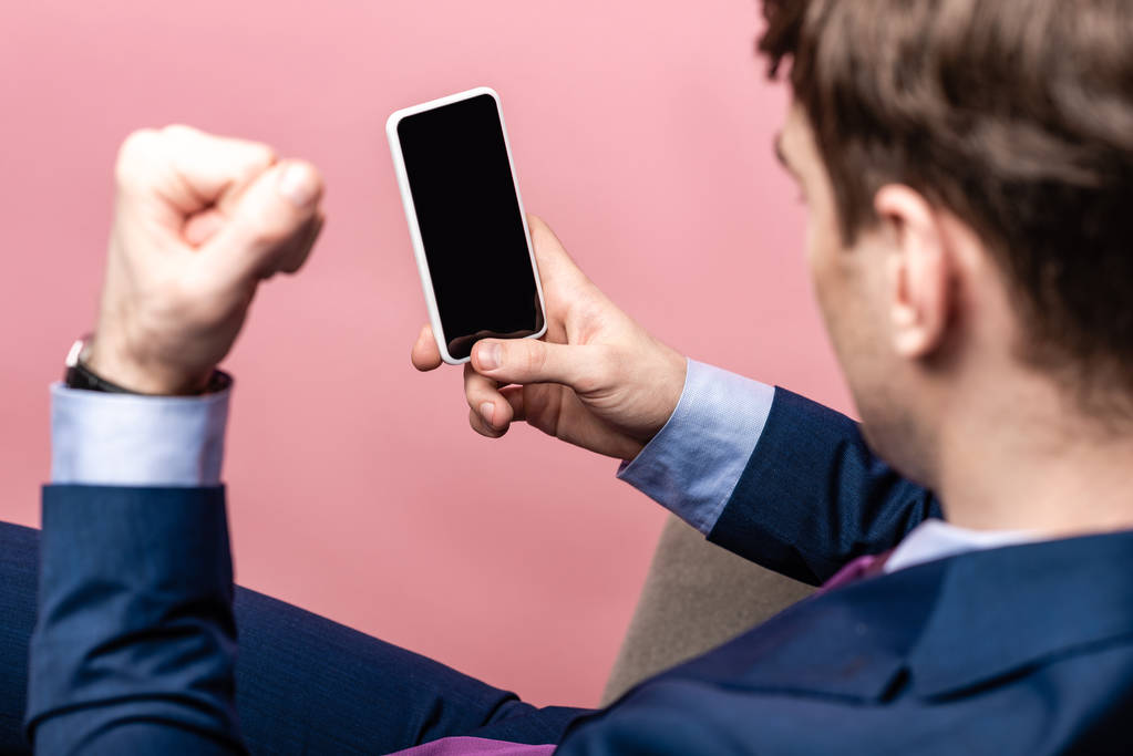 częściowy widok drażniąco biznesmen pokazując pięść trzymając smartfon z pustym ekranem izolowanym na różowym - Zdjęcie, obraz