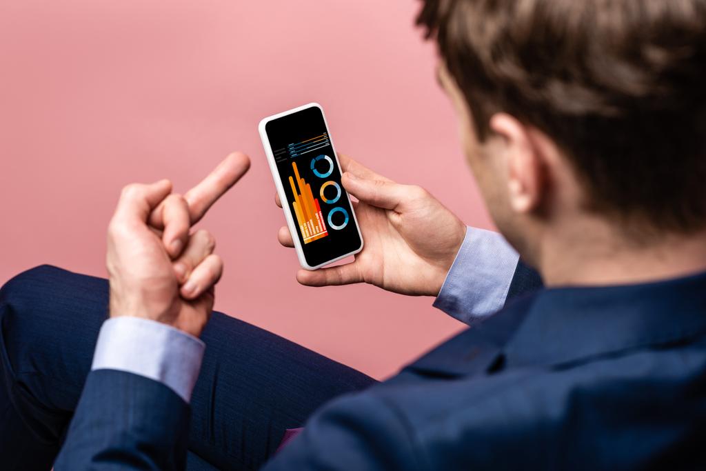 vista cortada de empresário usando smartphone com infográfico ao mostrar o dedo médio, isolado em rosa
 - Foto, Imagem