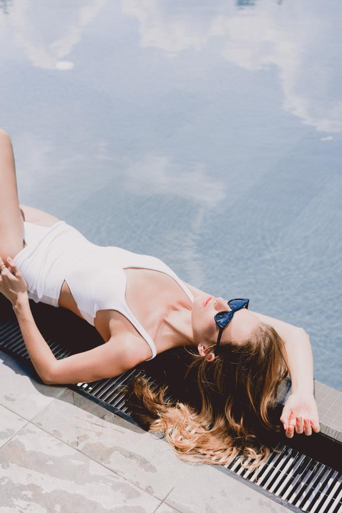 сексуальная блондинка в солнечных очках и в белых купальниках, лежащая возле бассейна под солнцем
 - Фото, изображение