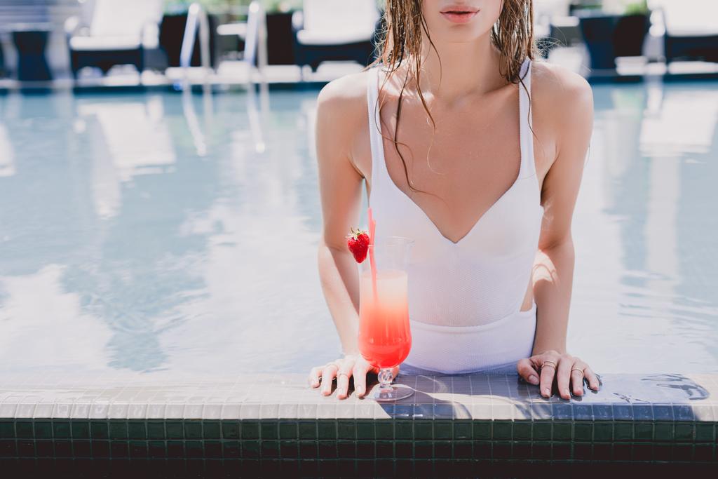 vista cortada da mulher molhada na piscina com cocktail de morango fresco
 - Foto, Imagem