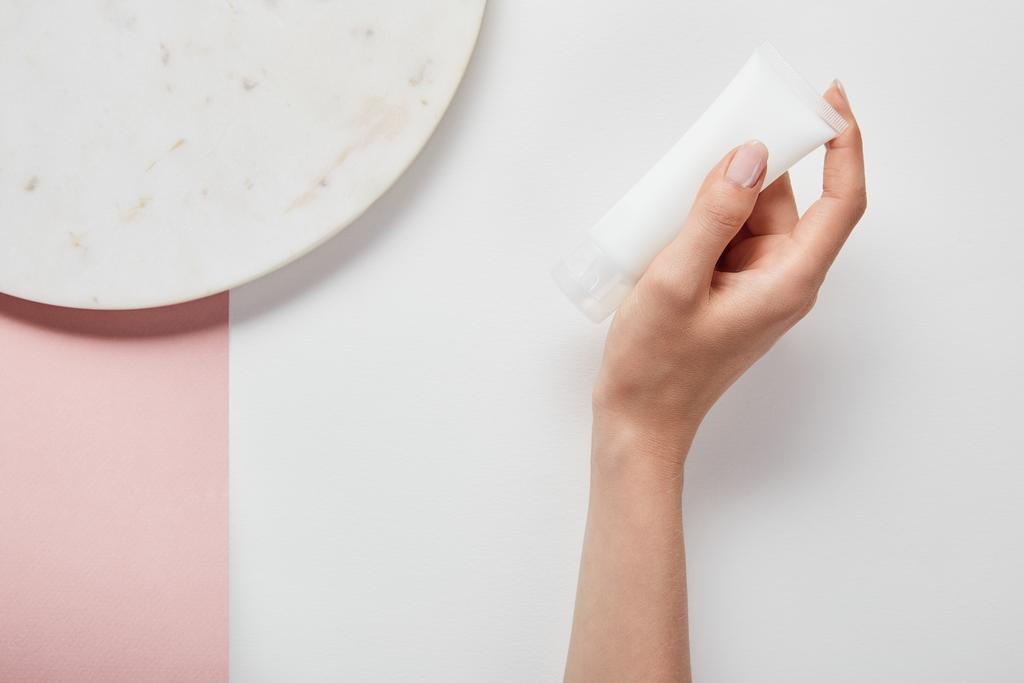 vista ritagliata della donna che tiene il tubo crema vicino al piatto sulla superficie rosa bianca
 - Foto, immagini