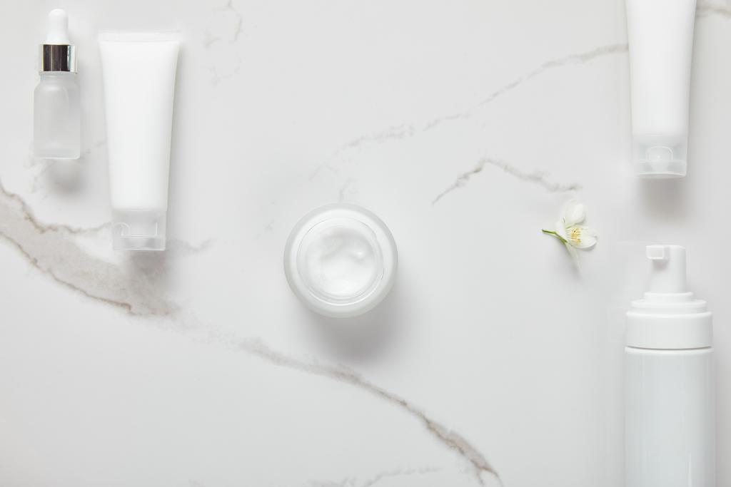 top view of cosmetic glass bottle, jar with cream, moisturizer tubes, dispenser and jasmine on white surface - Photo, Image