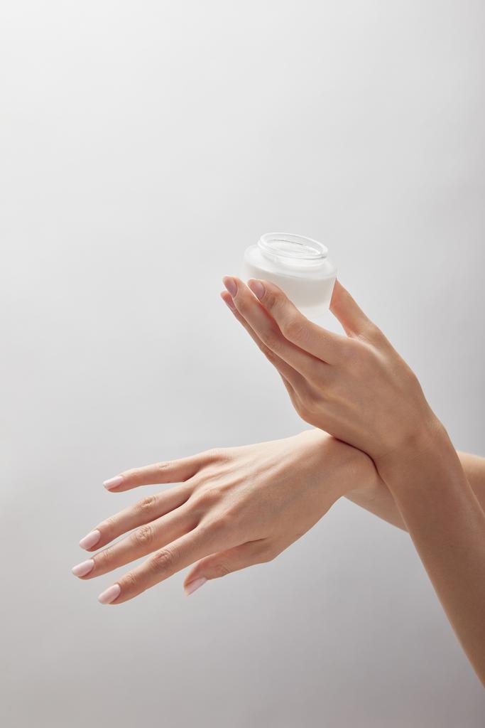 白に隔離されたクリームで瓶を持つ女性の手のトリミングビュー - 写真・画像