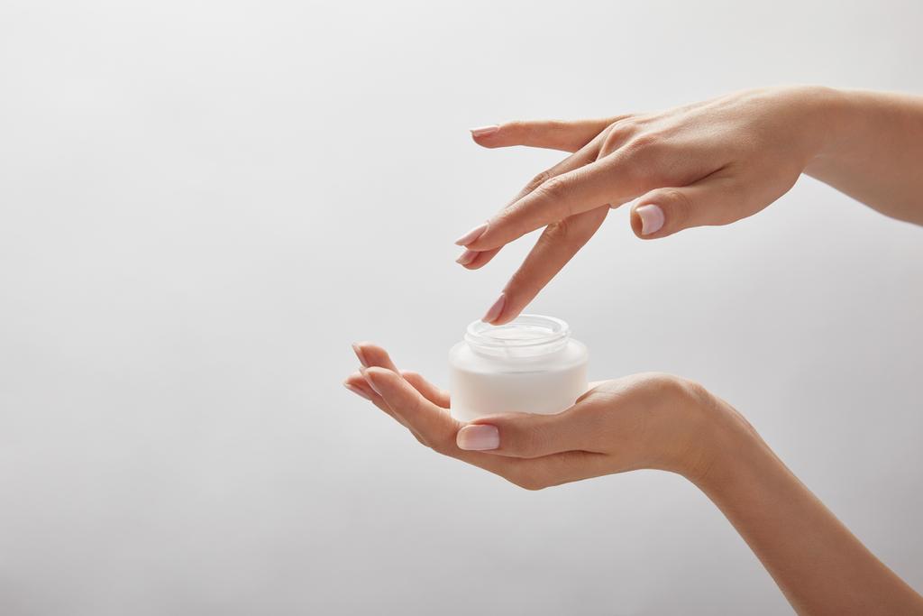 vista recortada de las manos de mujer sosteniendo frasco con crema aislada en blanco
 - Foto, Imagen