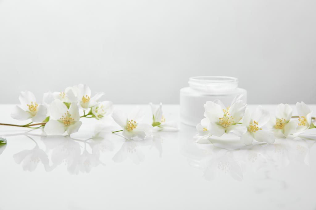 jasmine flowers on white surface near jar with cream - Photo, Image