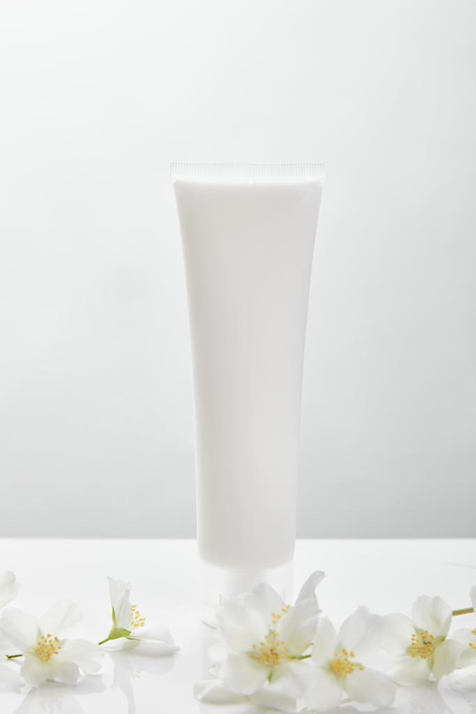 Jasmína na bílém povrchu v blízkosti kosmetické smetany v trubce - Fotografie, Obrázek