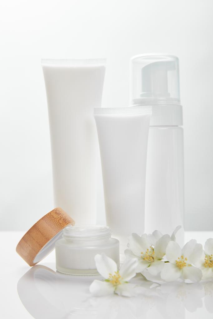 チューブ、瓶、化粧品ディスペンサーのクリームの近くの白い表面にジャスミンの花 - 写真・画像