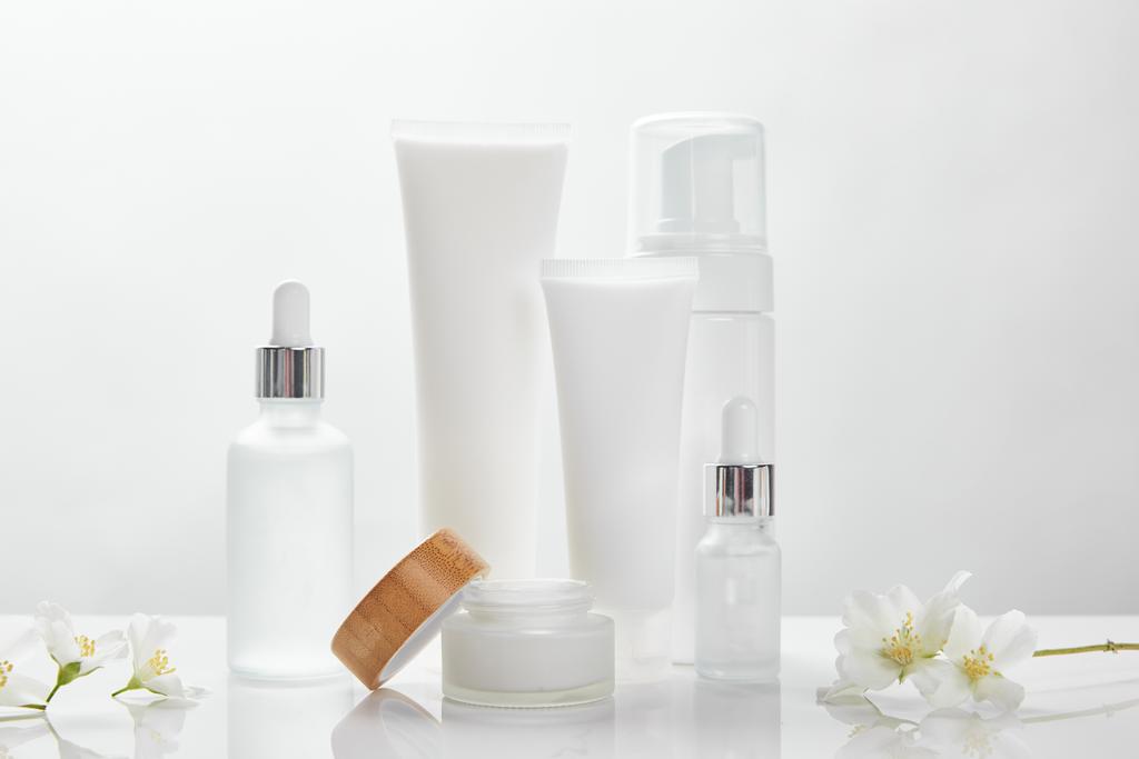 fleurs de jasmin sur la surface blanche près de bouteilles en verre, crème en tubes, pot et distributeur de cosmétiques
 - Photo, image