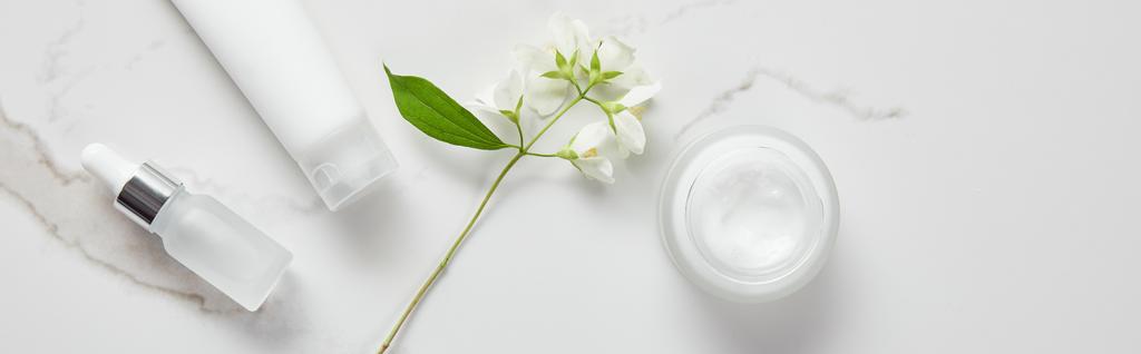 plan panoramique de jasmin, bouteille en verre cosmétique, pot avec crème et tube hydratant sur surface blanche
 - Photo, image