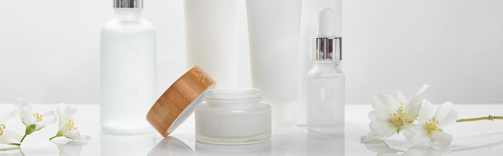 plan panoramique de crème en tubes, bocal et bouteilles en verre cosmétique avec jasmin sur surface blanche
 - Photo, image