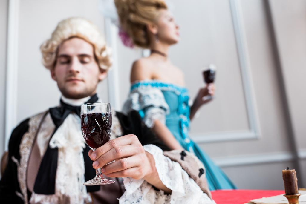 селективное внимание мужчины-победителя в парике, держащего стеклянное вино рядом с напыщенной женщиной
  - Фото, изображение