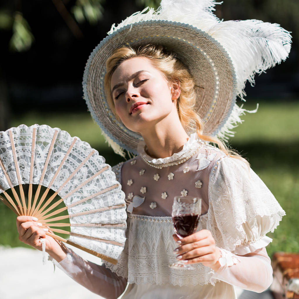 vrolijke jonge Victoriaanse vrouw die fan en wijn glas houdt  - Foto, afbeelding