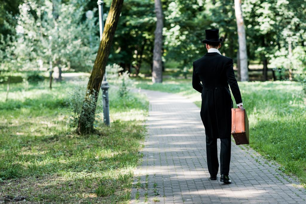 Вид сзади на человека в шляпе, который держит мешок и выходит на улицу
  - Фото, изображение