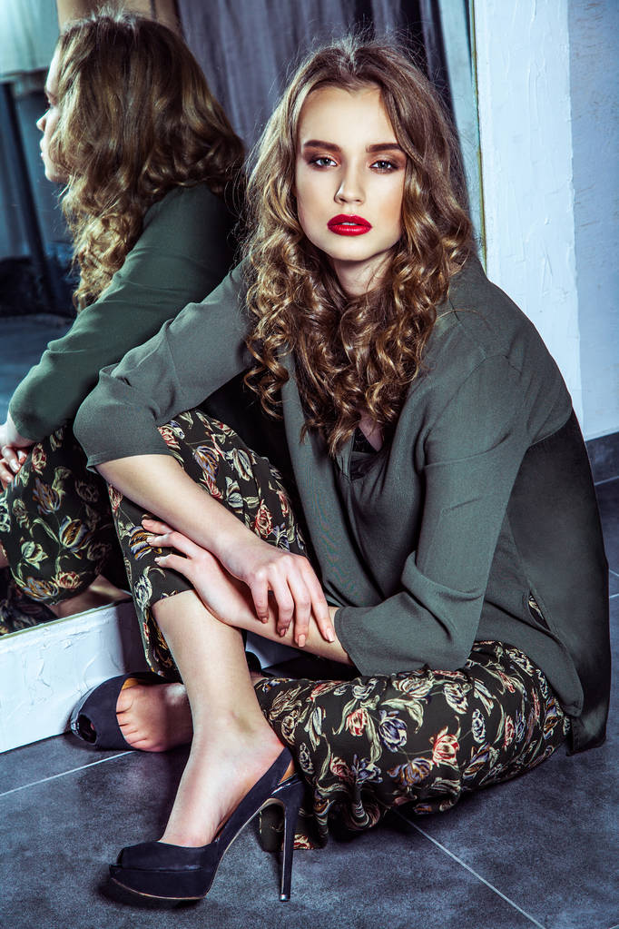 Model mody z makijażu i faliste fryzury opierając się na lustro i siedzi na podłodze w przymierzalni  - Zdjęcie, obraz