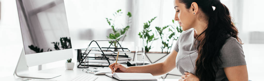 plan panoramique de la femme enceinte assise derrière la table avec ordinateur, clavier et plateau de documents, notes d'écriture et ventre
  - Photo, image